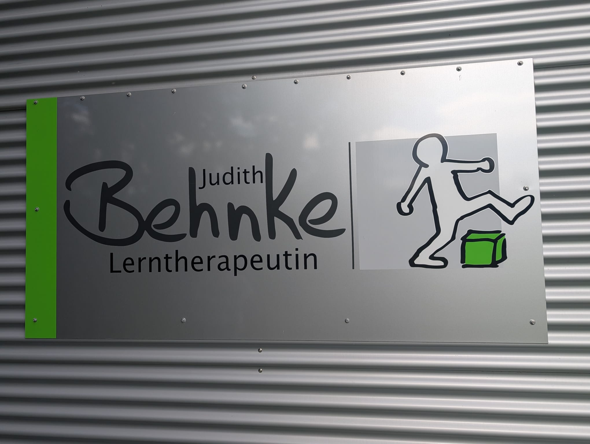 Nahaufnahme des Praxisschilds: der Schriftzug „Judith Behnke – Lerntherapeutin“ mit der Figur, die über einen grünen Würfel steigt.