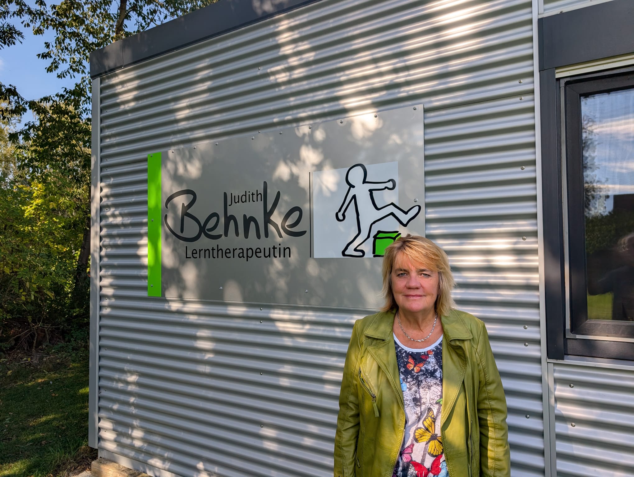 Judith Behnke vor ihrer Praxis, daneben das Schild „Judith Behnke – Lerntherapeutin“
