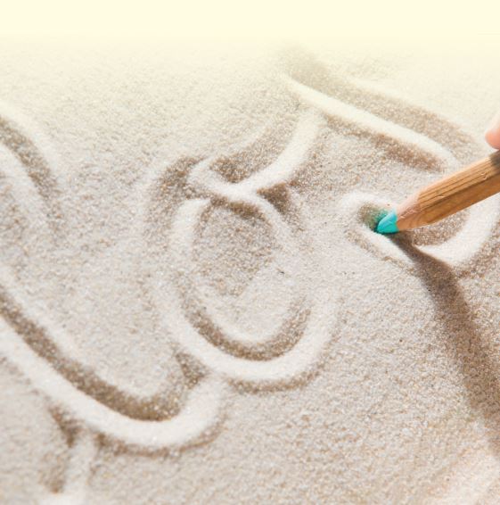 Ein Buntstift zeichnet Buchstaben in feinen Sand